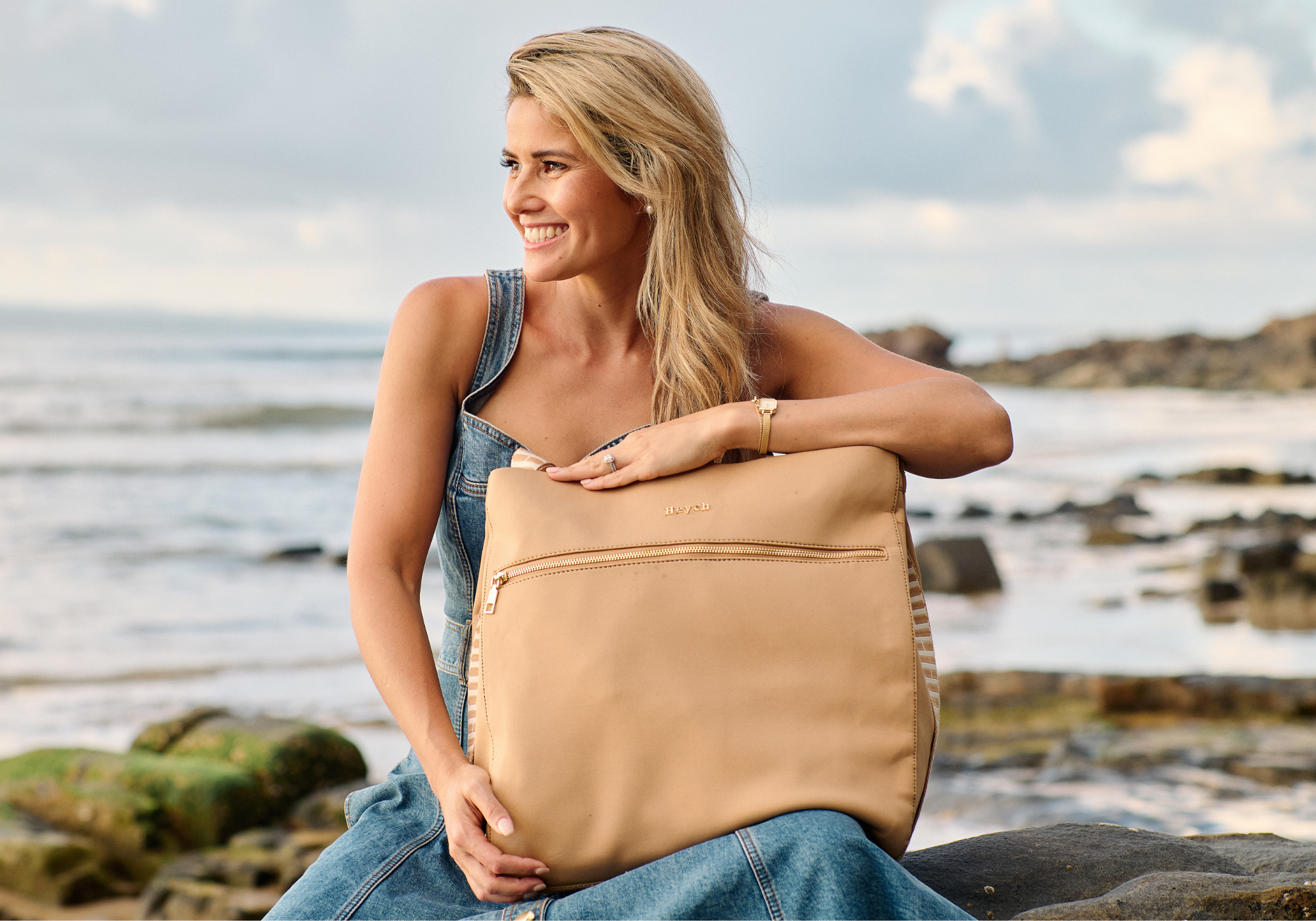 Designer and Founder Laura King holding Tan neoprene tote bag at the beach