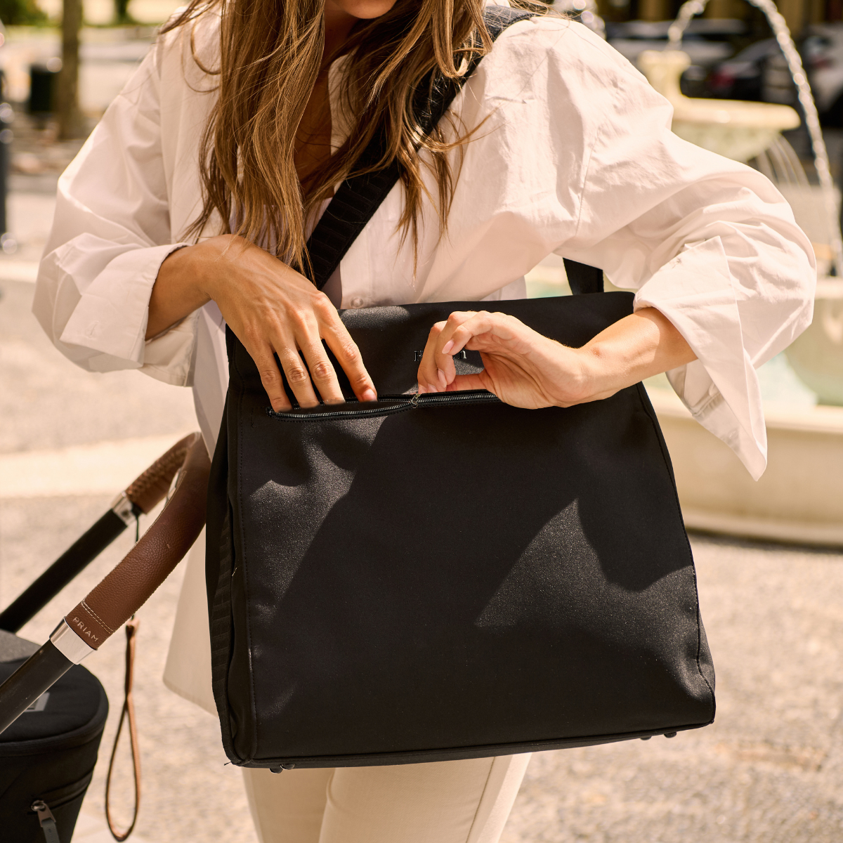 Mother standing next to pram unzipping black neoprene baby bag