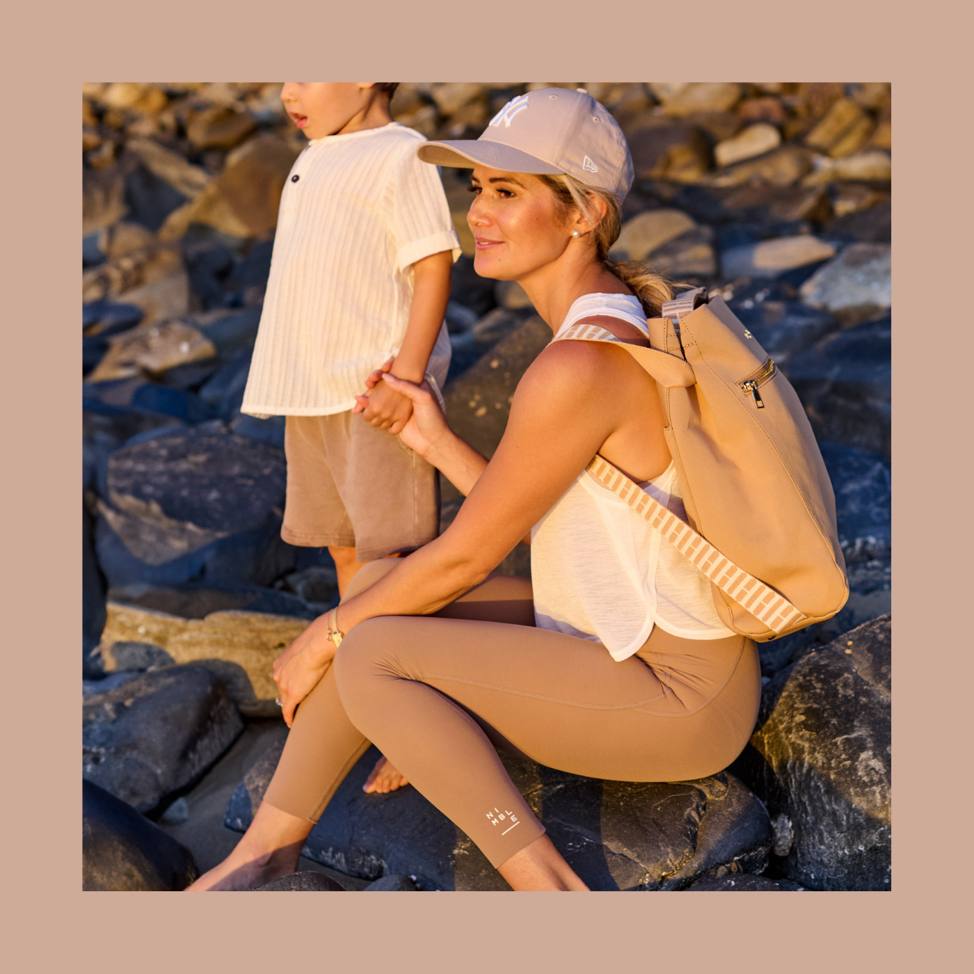 Mother sitting next to child on rocks at the beach with tan neoprene bag as a backpack